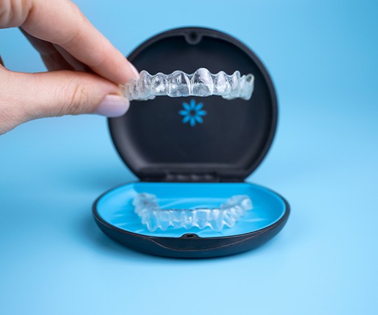 Woman’s hand lifting Invisalign out of its carrier case with light blue background