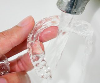 Closeup of fingers holding Invisalign under running water