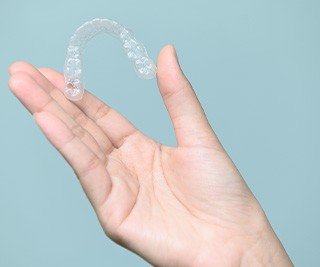 Hand holding Invisalign with light teal background