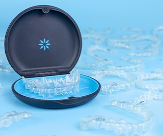 Multiple Invisalign trays surrounding ones in the carrier case with light blue background