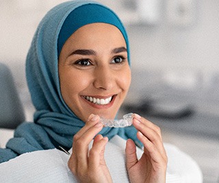 Woman in blue head wrap holding Invisalign sitting in dental chair