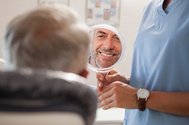 Man smiling at reflection in handheld mirror